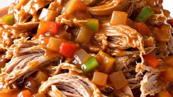 A close-up of tender, shredded pulled pork in a rich, dark red tomato sauce, served in a ceramic slow cooker.