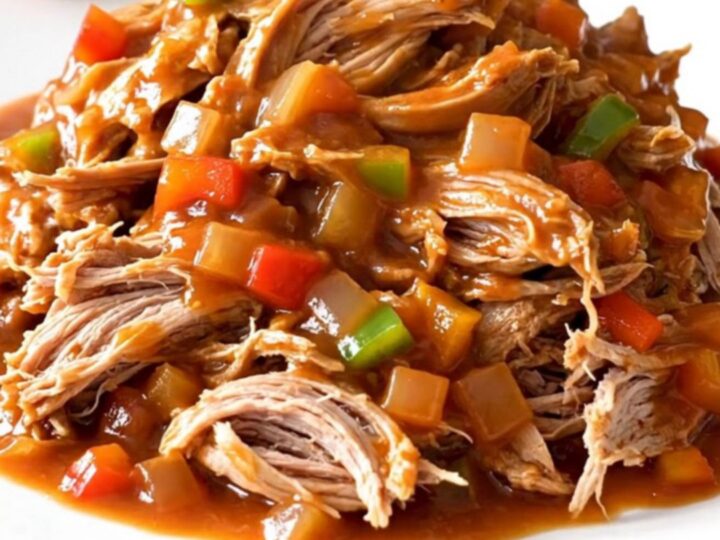 A close-up of tender, shredded pulled pork in a rich, dark red tomato sauce, served in a ceramic slow cooker.