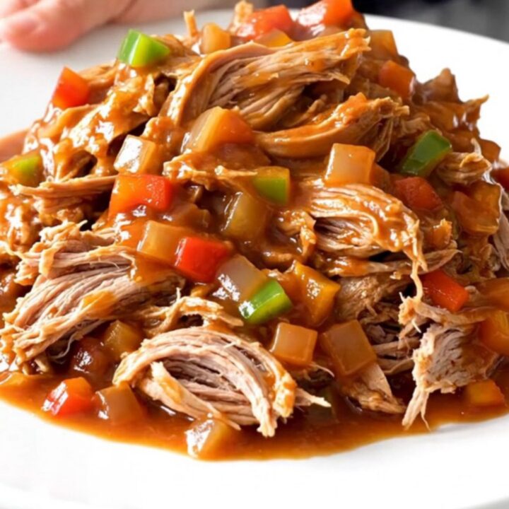A close-up of tender, shredded pulled pork in a rich, dark red tomato sauce, served in a ceramic slow cooker.