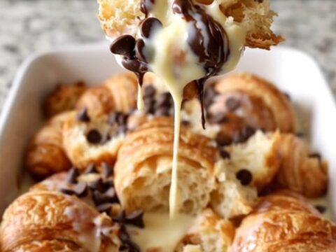 A large white rectangular dish filled with baked golden-brown croissant bread pudding with melted chocolate chips.