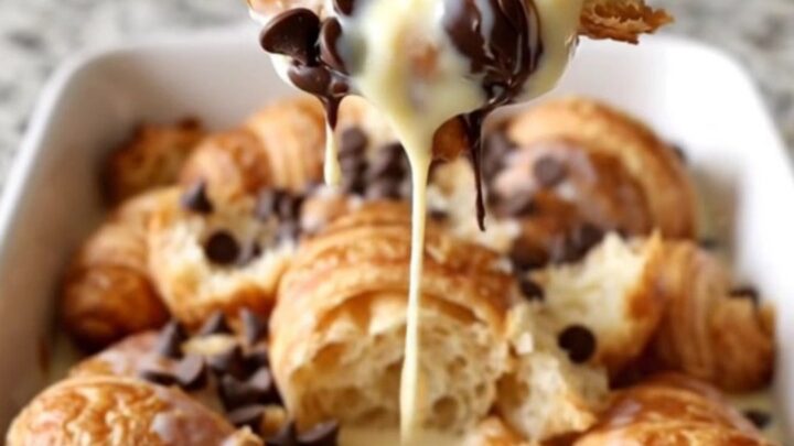 A large white rectangular dish filled with baked golden-brown croissant bread pudding with melted chocolate chips.