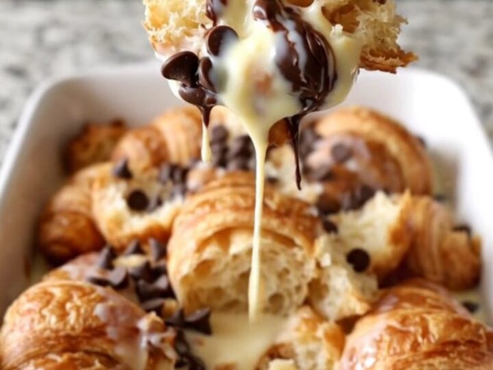 A large white rectangular dish filled with baked golden-brown croissant bread pudding with melted chocolate chips.