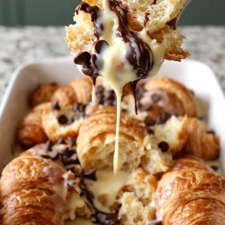 A large white rectangular dish filled with baked golden-brown croissant bread pudding with melted chocolate chips.