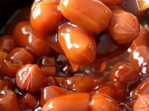 A close-up view of slow cooker pineapple sweet and sour hot dog bites with visible pineapple and pepper chunks.