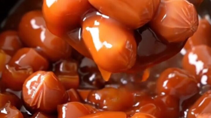 A close-up view of slow cooker pineapple sweet and sour hot dog bites with visible pineapple and pepper chunks.