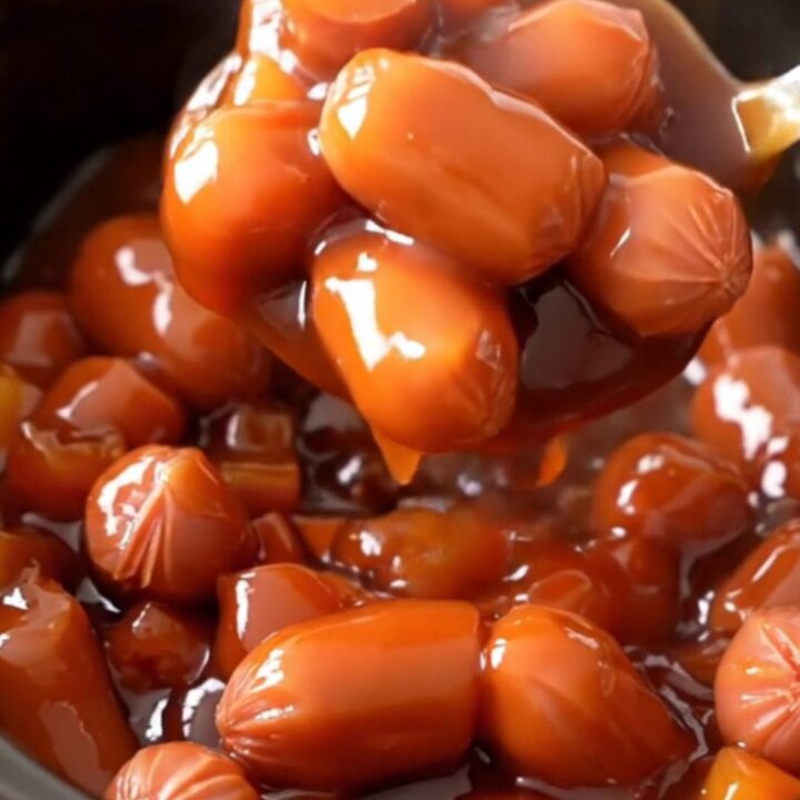 A close-up view of slow cooker pineapple sweet and sour hot dog bites with visible pineapple and pepper chunks.