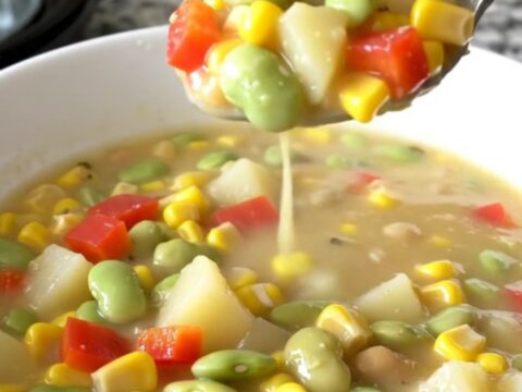 A shallow white bowl filled with creamy succotash chowder featuring corn, beans, and potatoes.