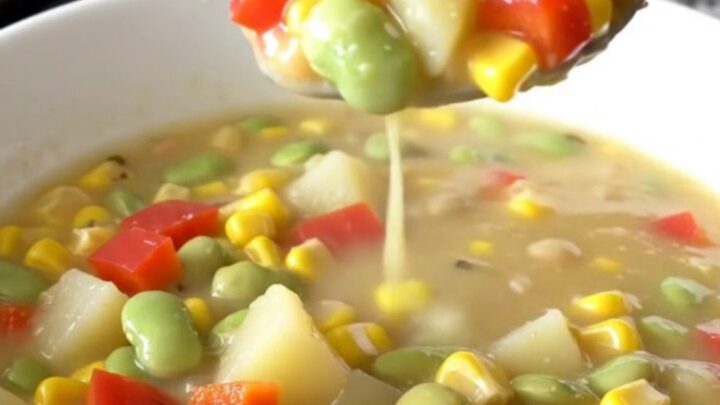 A shallow white bowl filled with creamy succotash chowder featuring corn, beans, and potatoes.