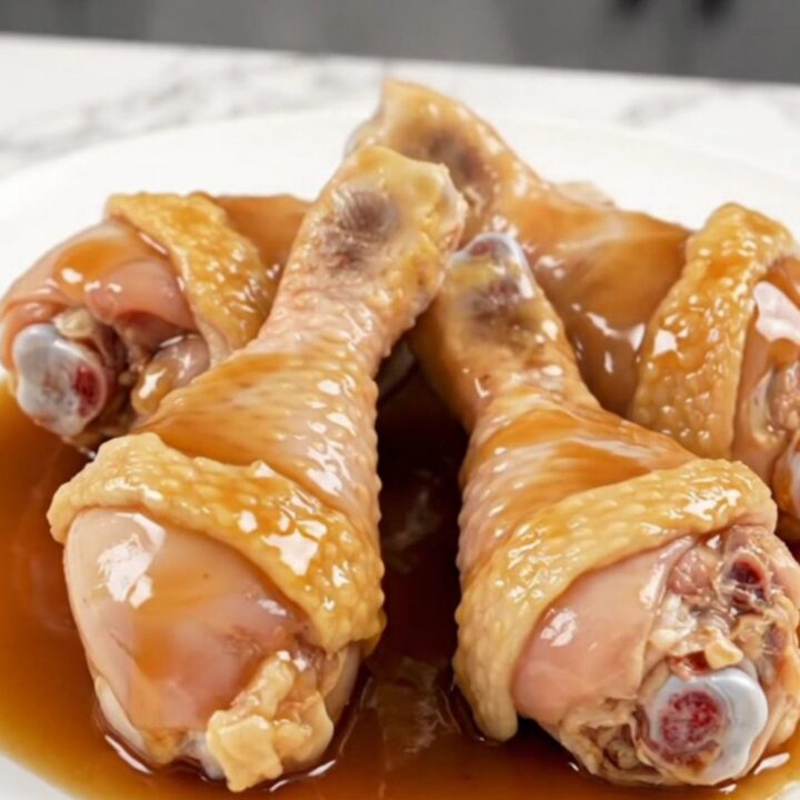 A close-up of maple garlic chicken drumsticks served on a white plate with a glossy, dark sauce.