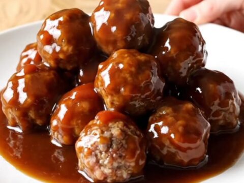 A close-up view of beef meatballs in a slow cooker, coated in a thick, glossy brown sugar and garlic glaze.