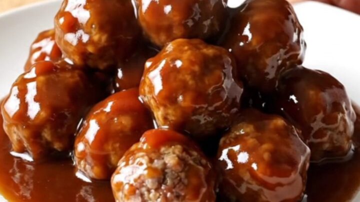 A close-up view of beef meatballs in a slow cooker, coated in a thick, glossy brown sugar and garlic glaze.