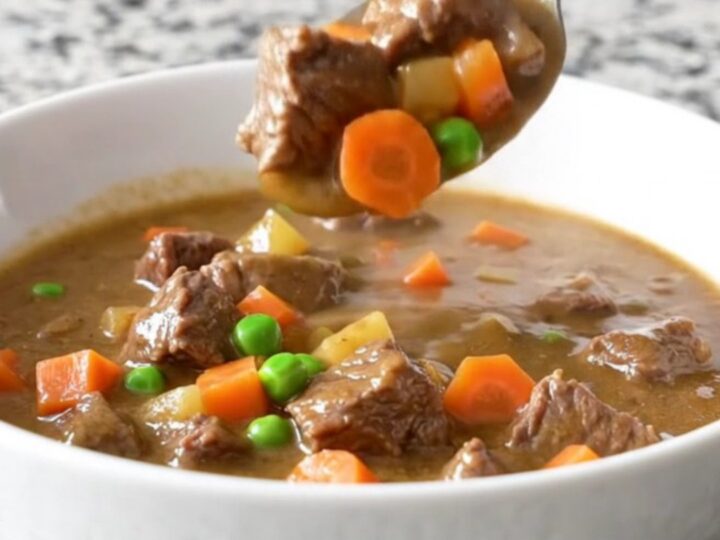 A close-up of a white bowl filled with creamy beef pot pie stew featuring tender beef cubes, potatoes, peas, and carrots.