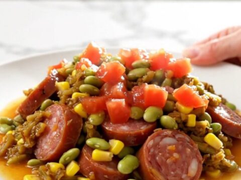 A top-down view of a slow cooker filled with colorful smoked sausage, corn, and lima beans in a savory tomato sauce.