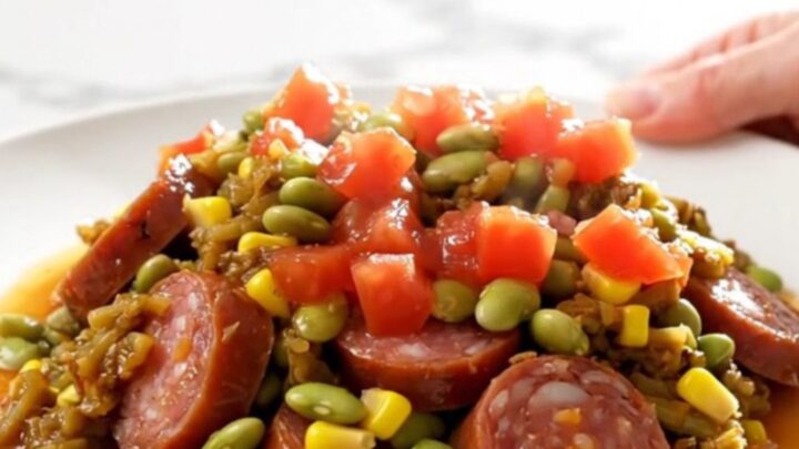A top-down view of a slow cooker filled with colorful smoked sausage, corn, and lima beans in a savory tomato sauce.