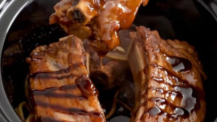 A close-up of tender boneless country-style pork ribs coated in a rich, dark honey balsamic glaze in a slow cooker.