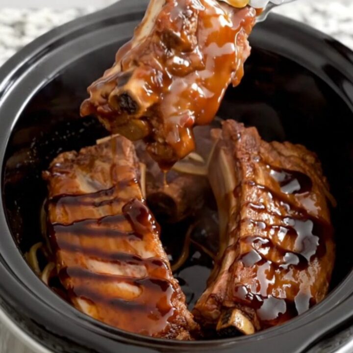 A close-up of tender boneless country-style pork ribs coated in a rich, dark honey balsamic glaze in a slow cooker.