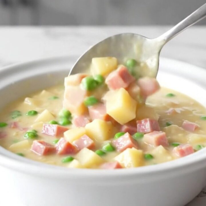 A bowl of creamy ham and potato chowder with visible cubes of ham, tender gold potatoes, and bright green peas.