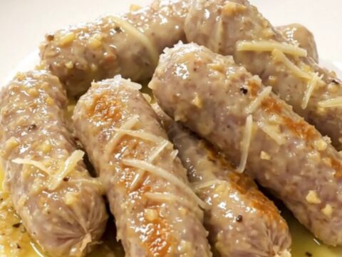 A close-up view of bratwurst and baby gold potatoes in a slow cooker, coated in a garlic Parmesan butter sauce.