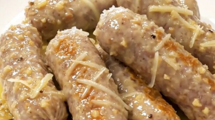 A close-up view of bratwurst and baby gold potatoes in a slow cooker, coated in a garlic Parmesan butter sauce.