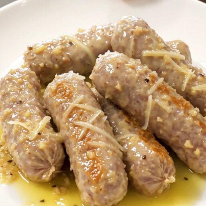 A close-up view of bratwurst and baby gold potatoes in a slow cooker, coated in a garlic Parmesan butter sauce.