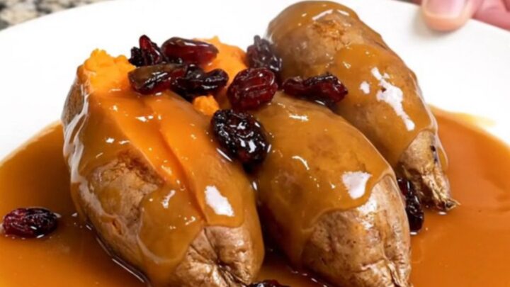 A close-up of tender, shingled sweet potato rounds in a slow cooker, glazed with a glossy orange and cranberry sauce.