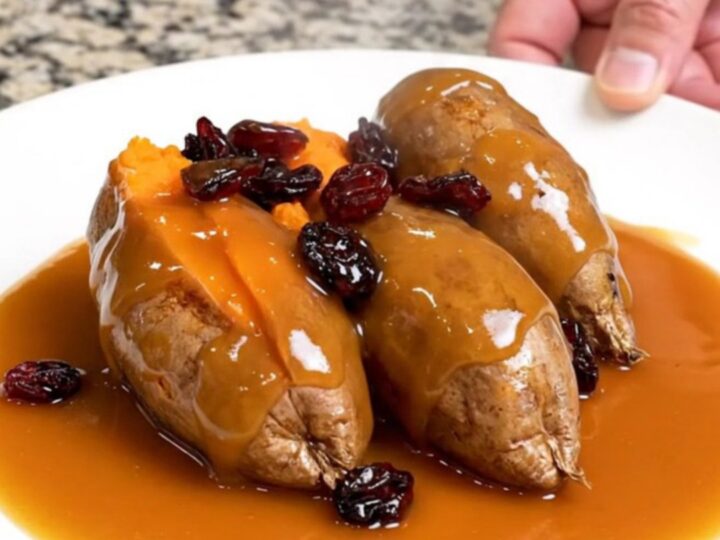 A close-up of tender, shingled sweet potato rounds in a slow cooker, glazed with a glossy orange and cranberry sauce.