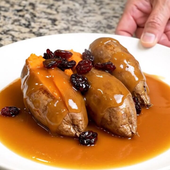 A close-up of tender, shingled sweet potato rounds in a slow cooker, glazed with a glossy orange and cranberry sauce.