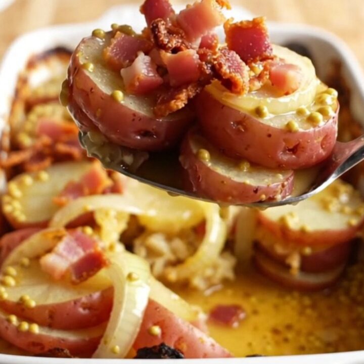 A rustic ceramic dish filled with sliced red potatoes, onions, and crispy bacon, fresh from the oven.
