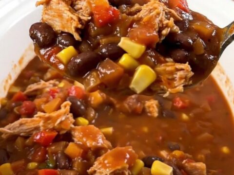 A steaming bowl of turkey chili with black beans and corn, topped with a hint of fresh cilantro on a rustic wooden table.