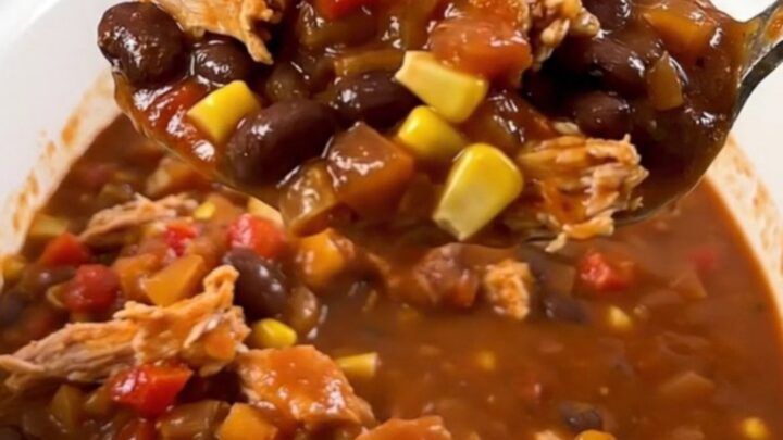 A steaming bowl of turkey chili with black beans and corn, topped with a hint of fresh cilantro on a rustic wooden table.