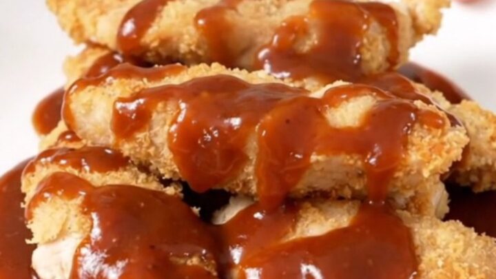 A close-up of tender, slow-cooked chicken strips coated in a glossy honey mustard barbecue sauce on a white plate.