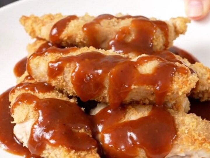 A close-up of tender, slow-cooked chicken strips coated in a glossy honey mustard barbecue sauce on a white plate.