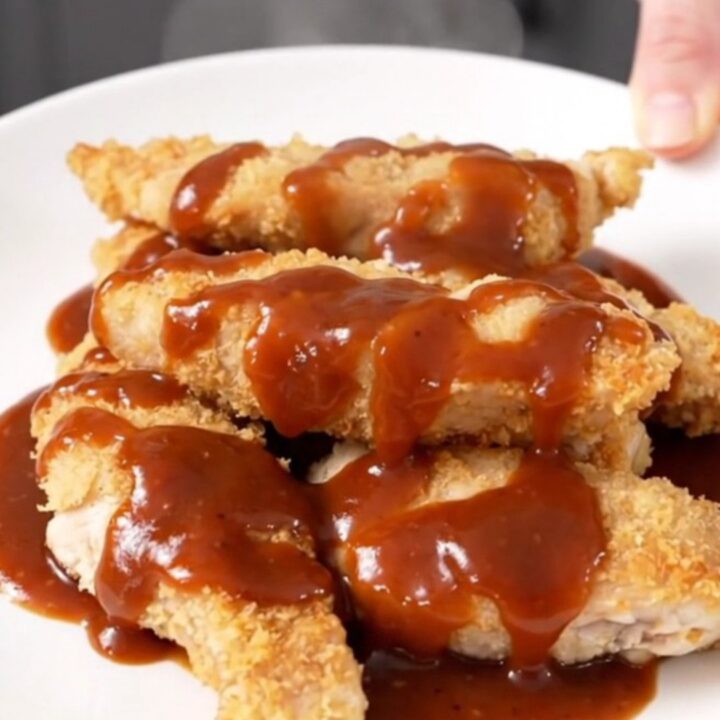 A close-up of tender, slow-cooked chicken strips coated in a glossy honey mustard barbecue sauce on a white plate.