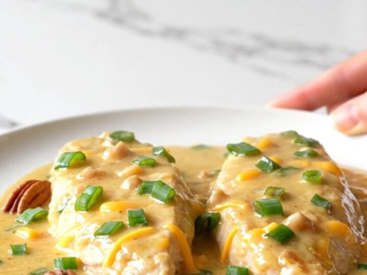 A slow cooker filled with creamy chicken breasts topped with pecans and green onions.