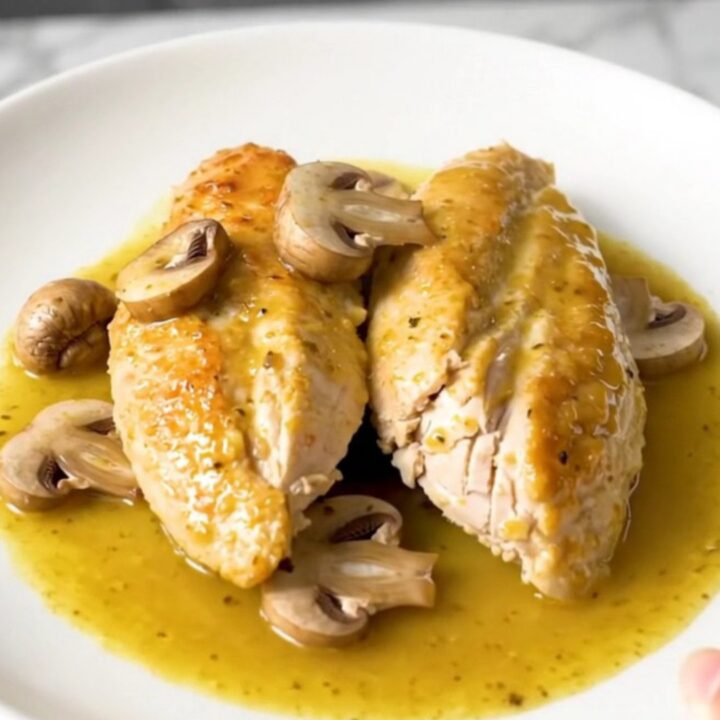 A close-up shot of slow-cooked chicken breasts smothered in a creamy Dijon mushroom sauce.
