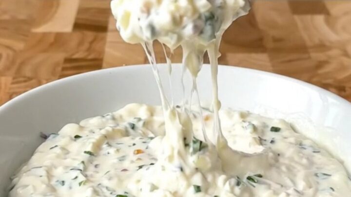 A white slow cooker filled with a creamy, melted garlic white pizza dip, garnished with herbs.