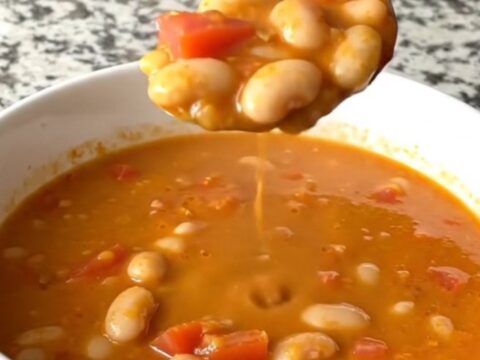 A rustic slow cooker filled with creamy tomato basil white bean soup on a speckled granite countertop.