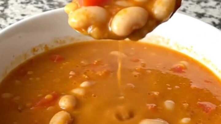 A rustic slow cooker filled with creamy tomato basil white bean soup on a speckled granite countertop.