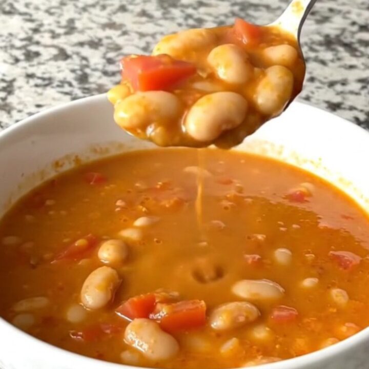 A rustic slow cooker filled with creamy tomato basil white bean soup on a speckled granite countertop.