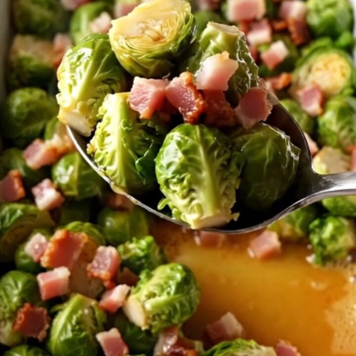 A large white rectangular baking dish filled with roasted Brussels sprouts and crispy bacon pieces.