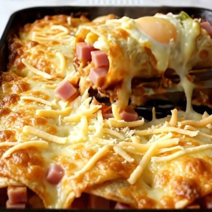 A top-down view of a rectangular ceramic baking dish filled with golden-brown breakfast enchiladas topped with melted cheese.