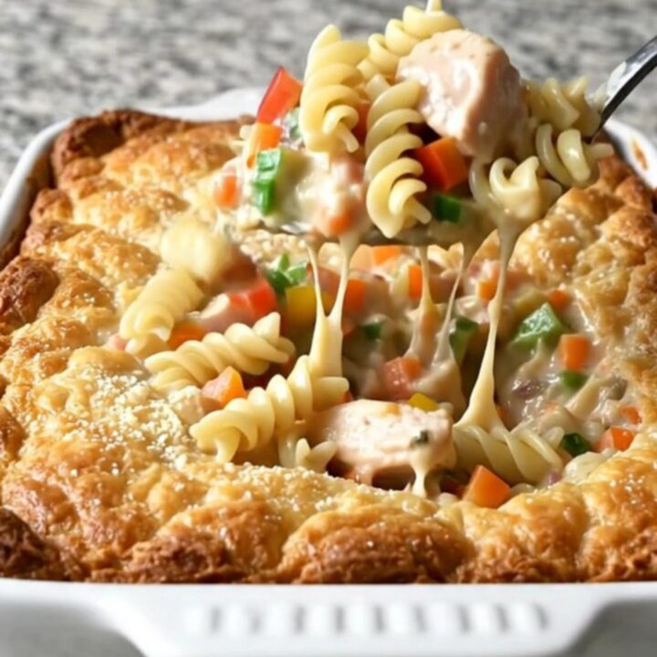 A top-down view of a creamy chicken primavera rotini bake in a white ceramic dish.
