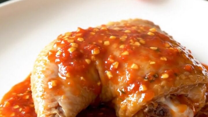 A close-up of tender, slow-cooked chicken leg quarters coated in a thick, glossy chili garlic sauce on a white plate.