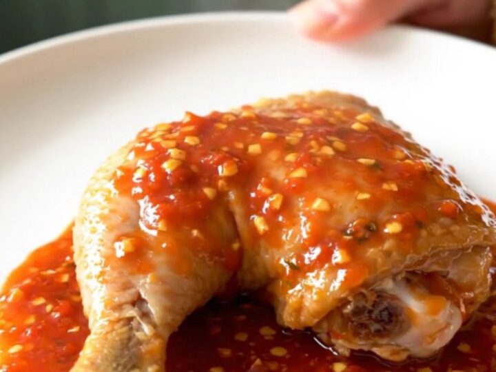 A close-up of tender, slow-cooked chicken leg quarters coated in a thick, glossy chili garlic sauce on a white plate.