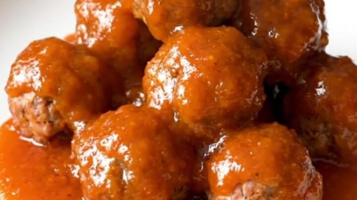 A close-up of a slow cooker filled with meatballs and cocktail sausages coated in a thick, glossy orange marmalade sauce.