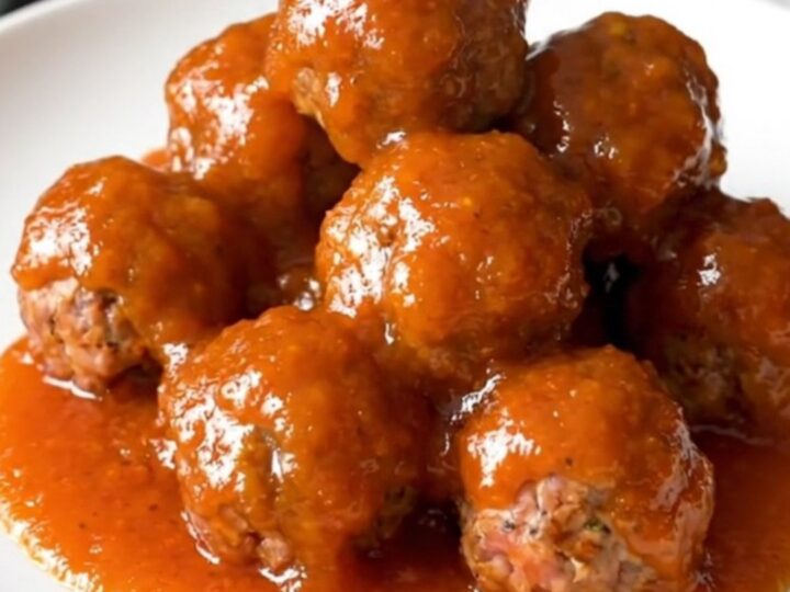 A close-up of a slow cooker filled with meatballs and cocktail sausages coated in a thick, glossy orange marmalade sauce.
