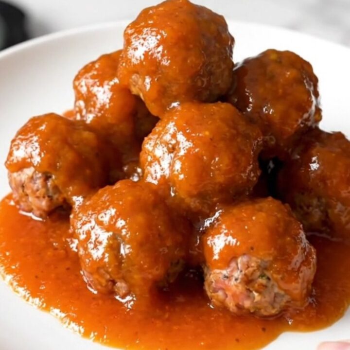 A close-up of a slow cooker filled with meatballs and cocktail sausages coated in a thick, glossy orange marmalade sauce.