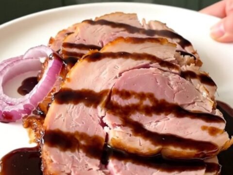 A beautifully glazed slow cooker ham sitting on a white plate, served with caramelized red onions.
