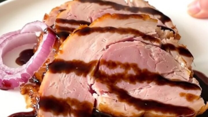 A beautifully glazed slow cooker ham sitting on a white plate, served with caramelized red onions.