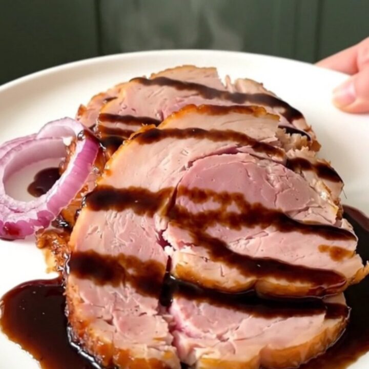 A beautifully glazed slow cooker ham sitting on a white plate, served with caramelized red onions.
